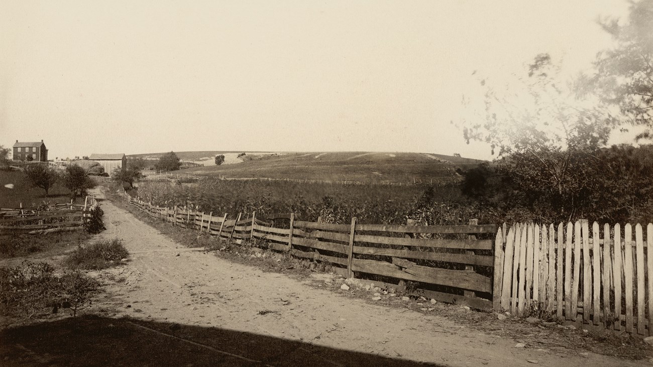 An 1885 photo shows a improved dirt road flanked by wood fences and farms.
