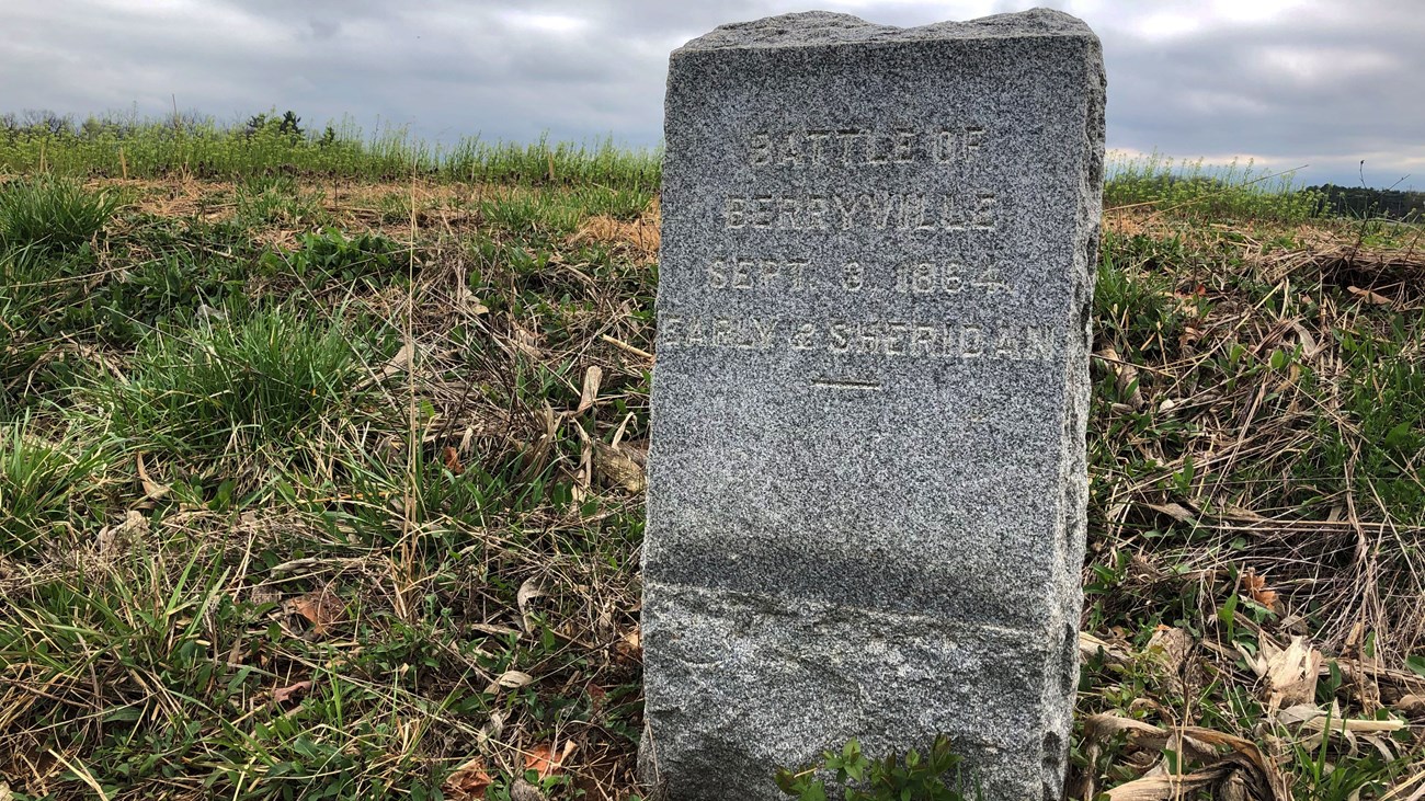 An engraved granite tablet marks the site of a battle on the a farm field behind it.