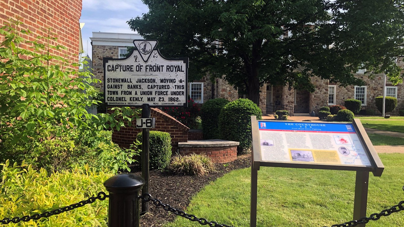 A highway historical marker and wayside exhibit stand on a courthouse grounds.