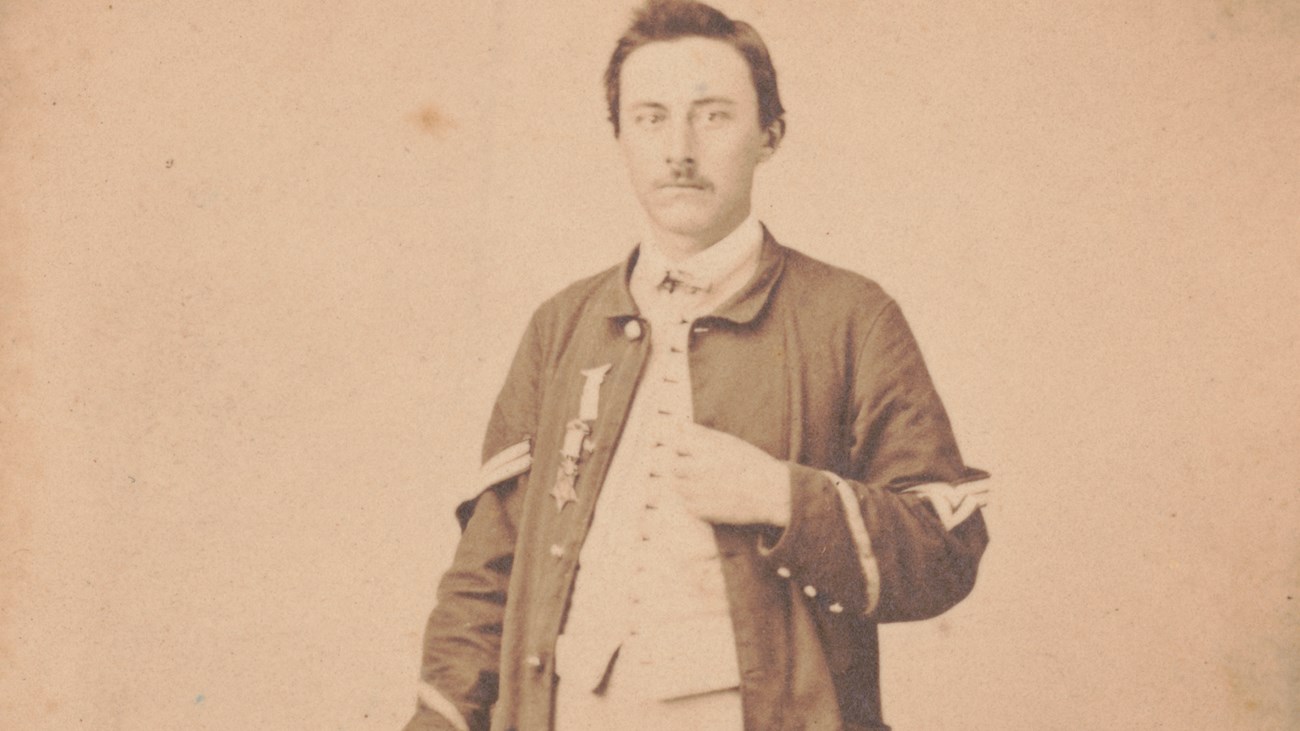 An 1864 photo is a portrait of a soldier posing with a medal on his coat.