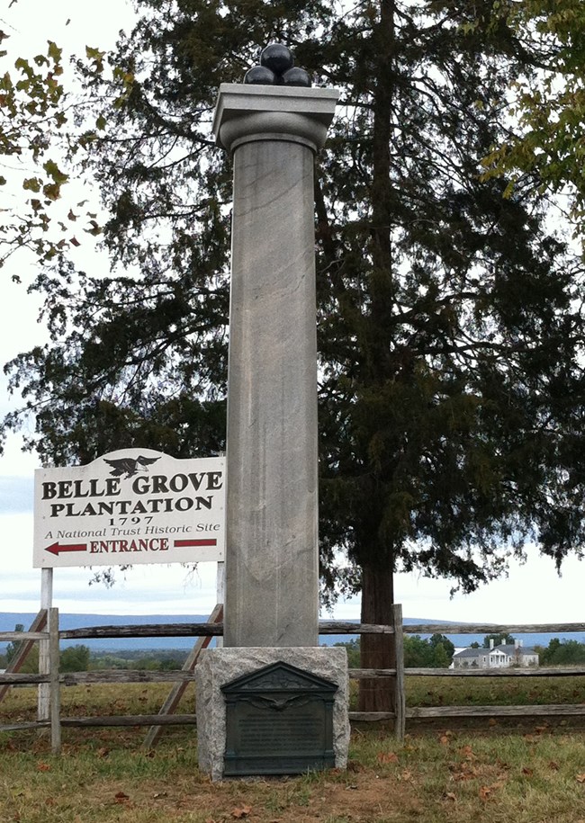 A stone column has four cannonballs atop its capitol and a bronze plaque at its base.