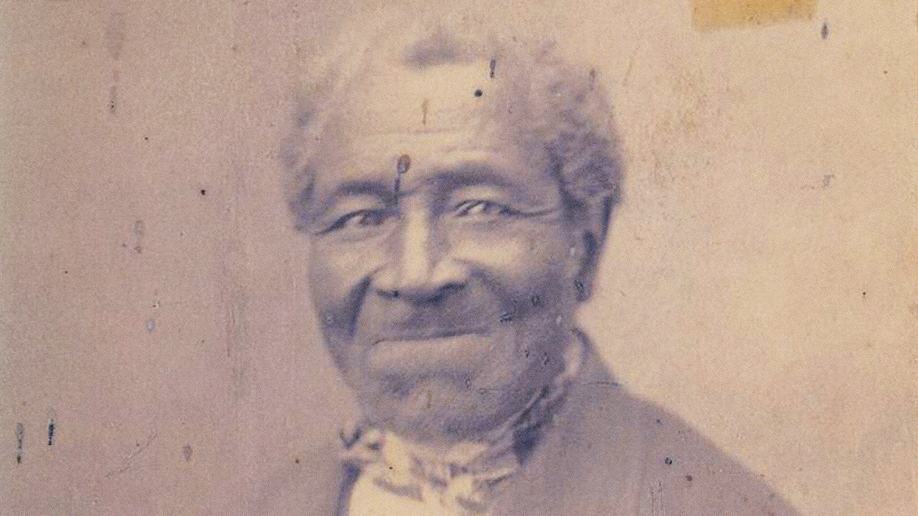 Steven A weathered 1800s portrait photo shows a grey haired man in a jacket and bow tie.