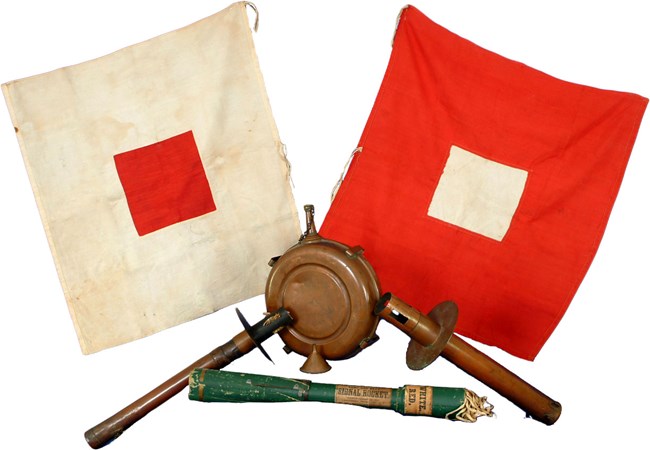 Square cloth flags from the 1800s with red and white patters are displayed with signal equipment.