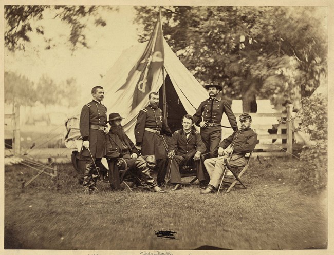 An 1864 photo depicts an army general flanked by his subordinate officers at his tent.