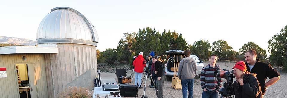Numerous people outdoors in front of an observatory with telescopes. Numerous people outdoors in front of an observatory with telescopes.