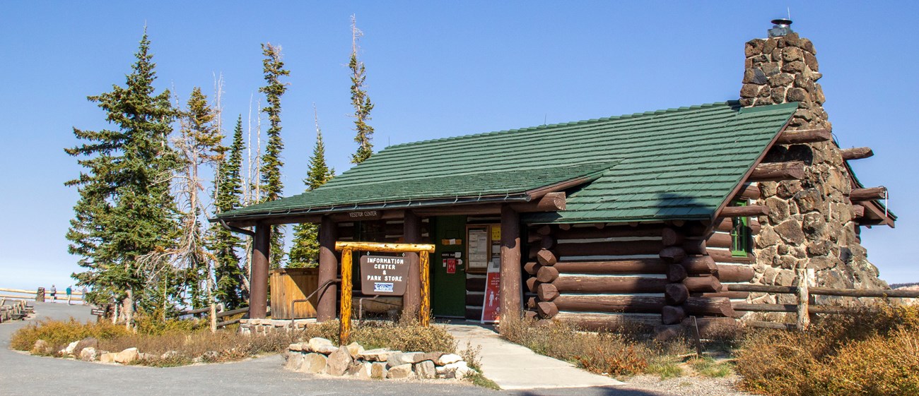 Modern image of a historic log cabin with a stone chimney on the end closest to the viewer.