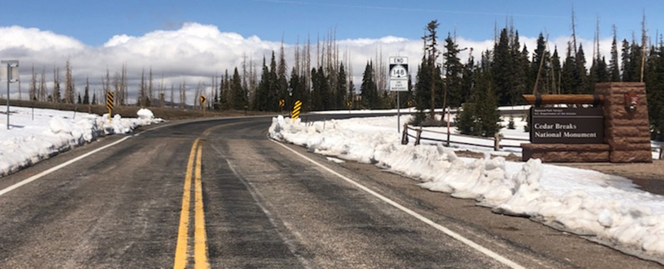 2022_RoadsOpen A two lane road leads passed a park sign, snow covers the ground on either side.