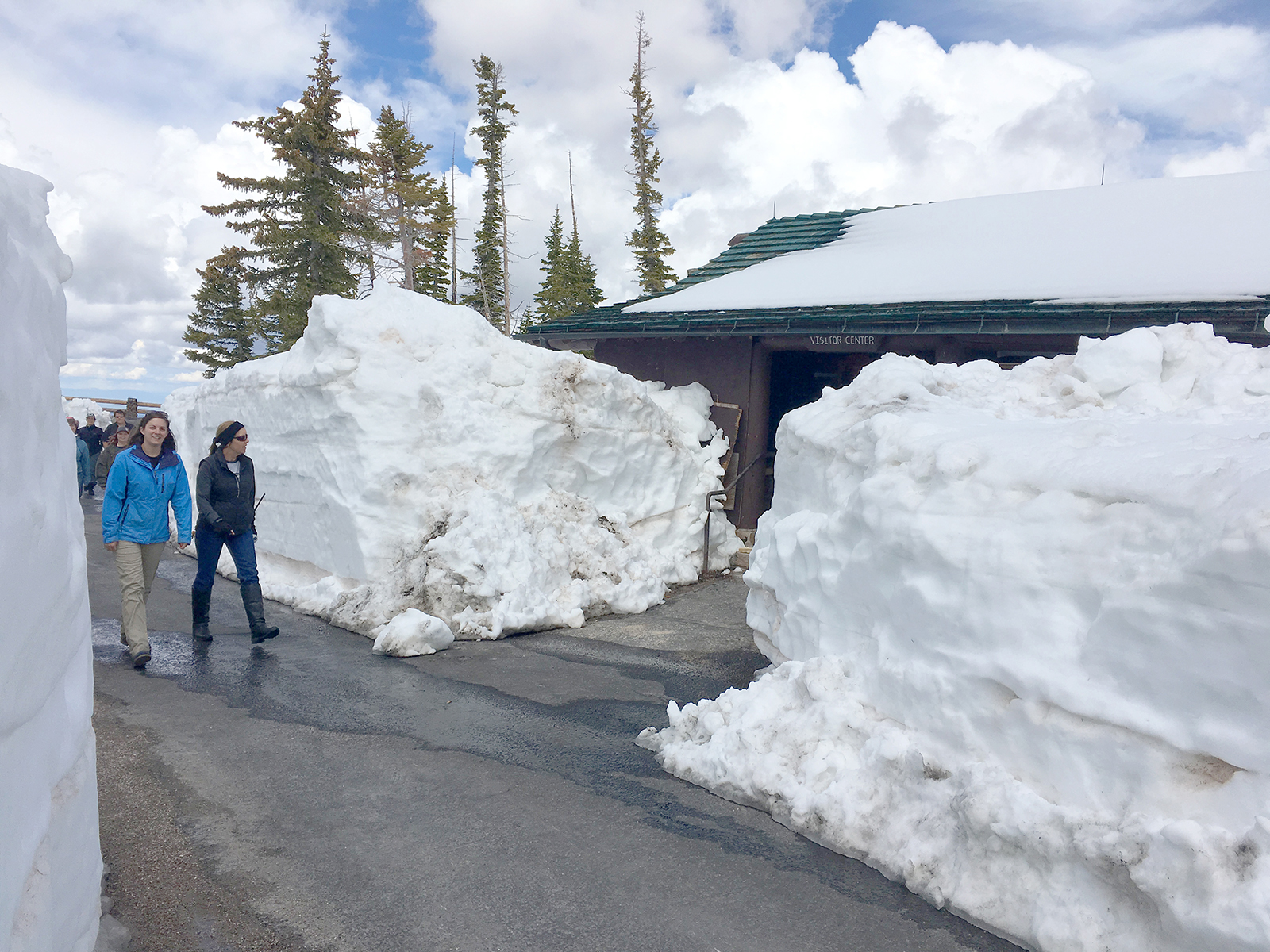 Snow at Visitors Center People walking by drifts of snow blocking a small log cabin.
