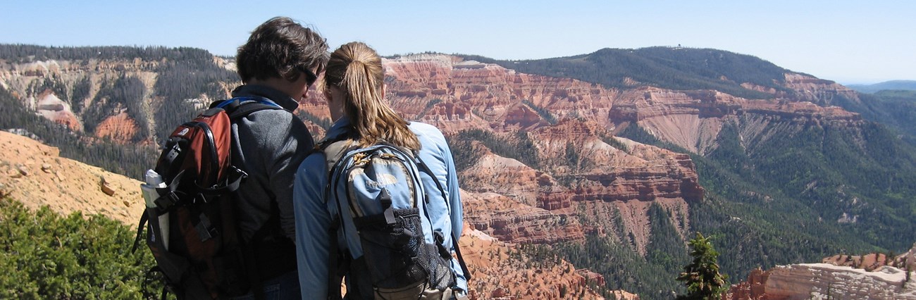 Two people facing away from the camera overlook a red rock formation.