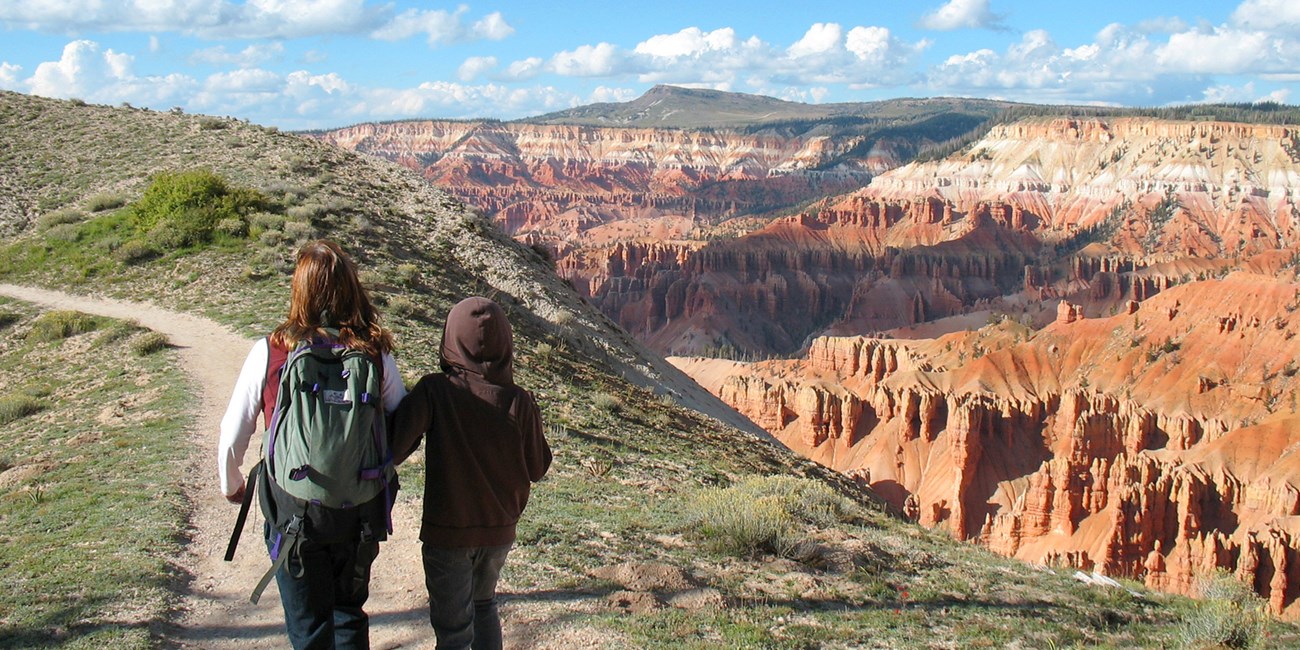 Two people hiking along the cliff rim of Cedar Breaks.
