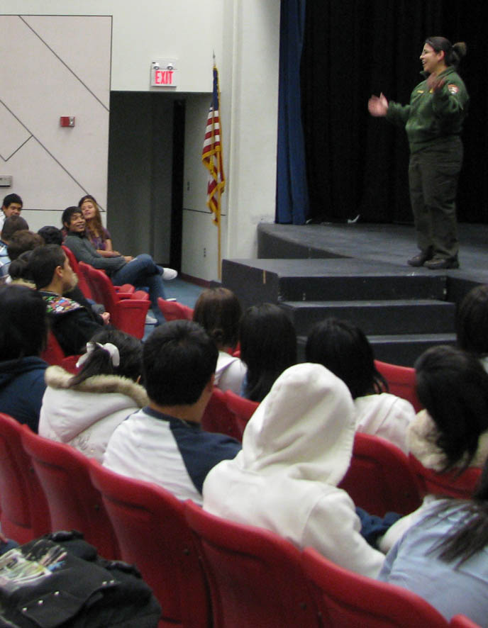 A ranger stands on stage facing a theater full of high school students.