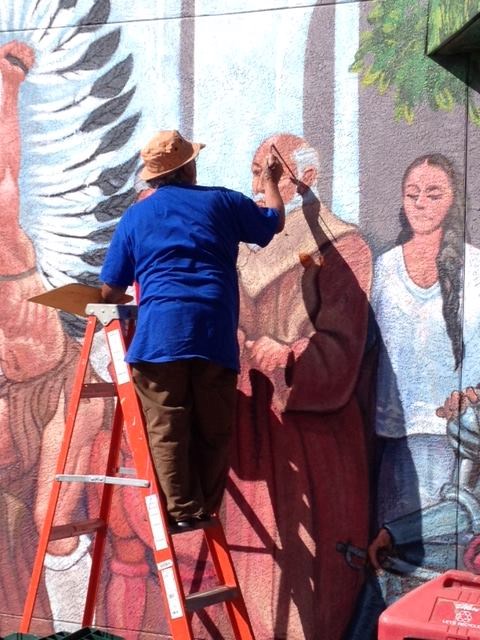 View of the back of a man on a ladder as he paints on the stucco wall of a building