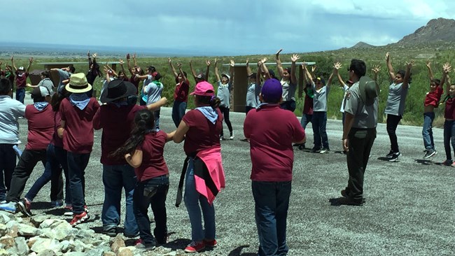 kids with arms in air, circled around park ranger