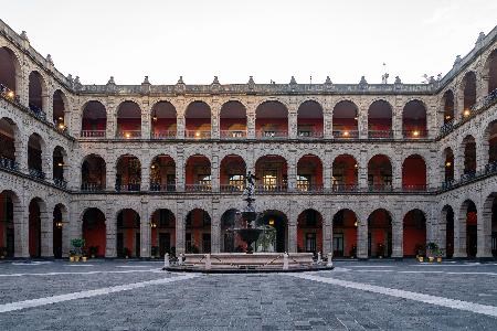 A three-story building surrounds an inner courtyard. Rows of arched openings line the exterior walls of each floor.