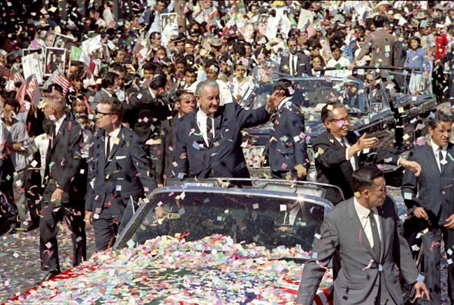 Presidents Johnson and Diaz Ordaz wave to crowd from open car. Confetti fills the air and hood of car.