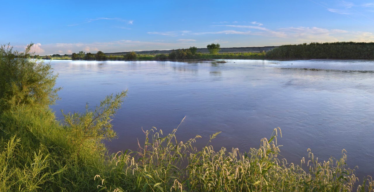 A wide, calm river flows between banks covered in low, green vegetation.