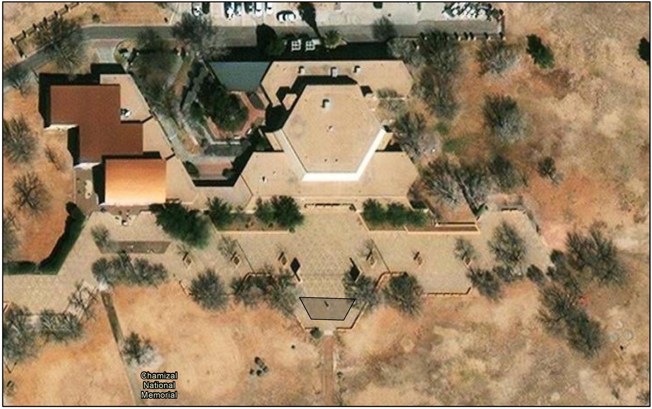 Aerial perspective of park cultural center and office building with paved area extending along the bottom side of them. A trapezoid-shaped area is highlighted on the paved walkway in front of the cultural center.