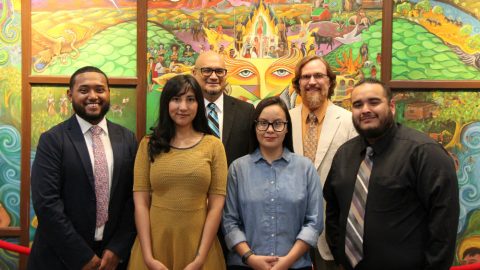 Cast of Ground Four men, two women standing in front of brightly-colored mural facing you