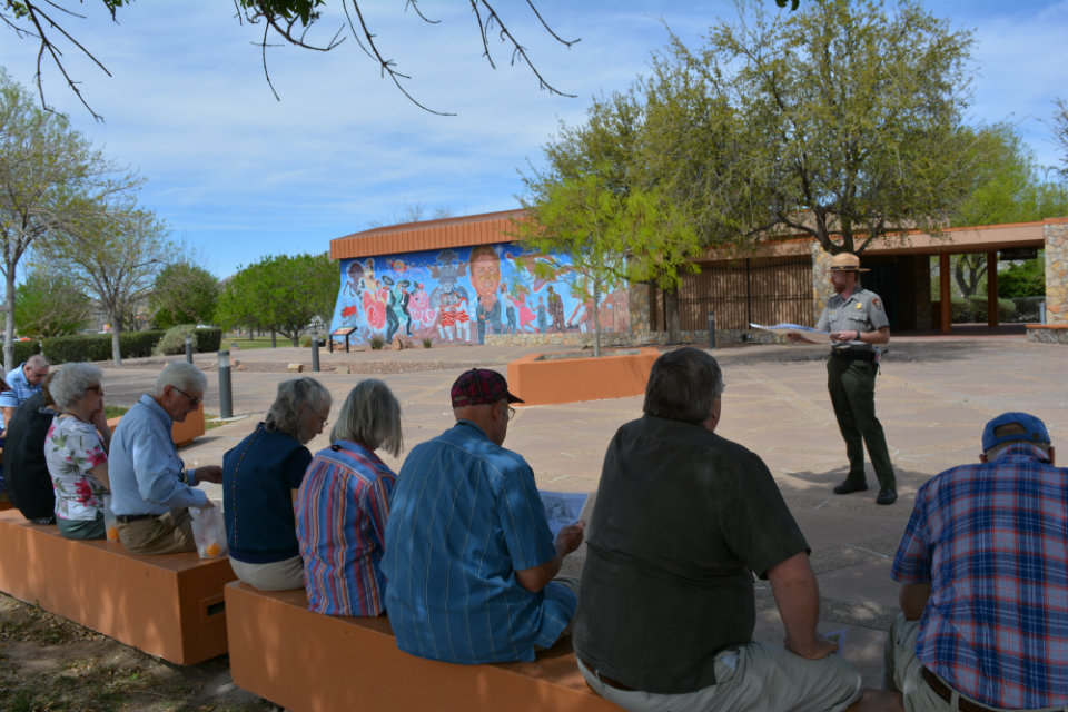 a view of a row of people sitting outside on benches facing a park ranger