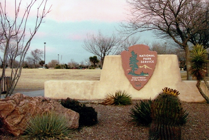 Chamizal National Memorial entrance gate stucco wall at entrance gate displays large NPS arrowhead logo, desert plants growing at its base