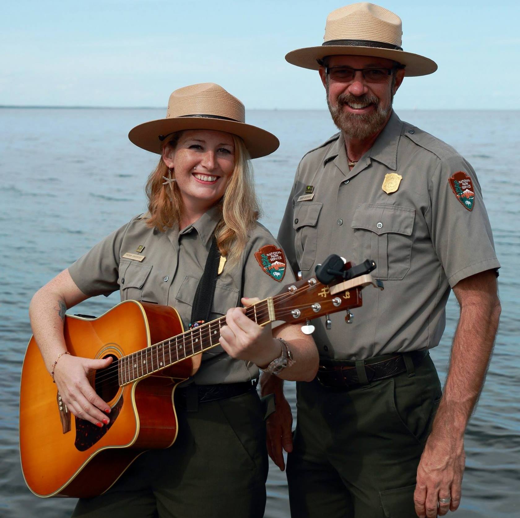 Woman holding guitar and man, both in park ranger uniforms