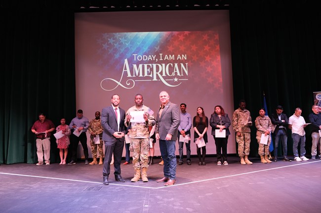 Many people standing on stage celebrating new citizenship.