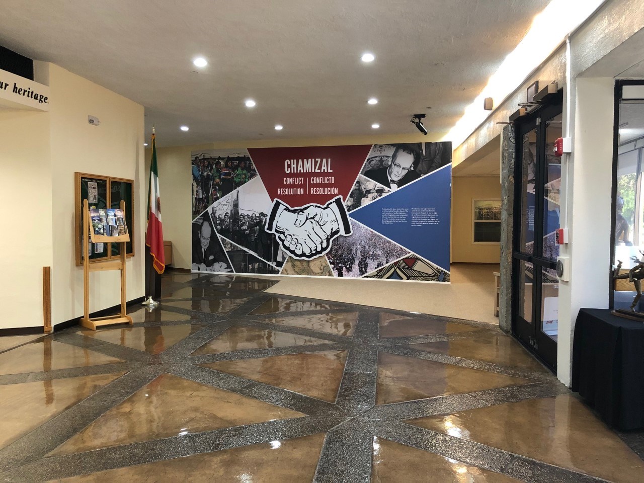 A wall mural with a collage of images marks the exhibit entrance across an open lobby.