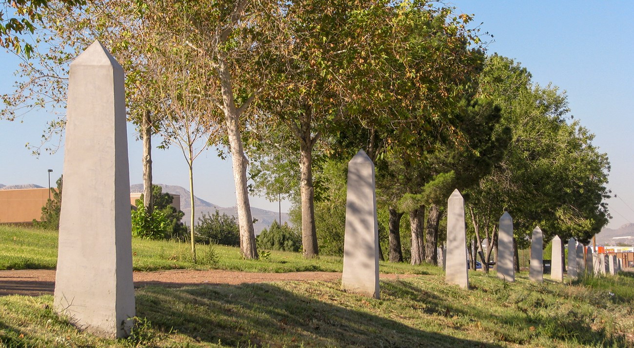A row of white, cement, obelisk-shaped posts stretches into the distance along a walking path.
