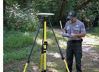 Park employee with a tripod set up along a gravel road performing boundary surveying task.