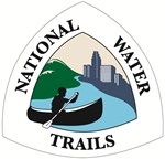 Silhouette of paddler on blue river, green forest on river left and city skyline on river right. Wording around edge is National Water Trail.