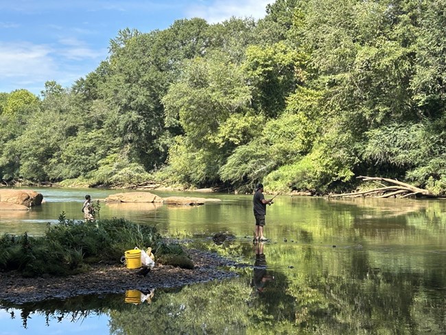 Two people fishing from shallow water shoals in the river.