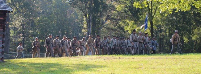Living historians portraying Confederate soldiers during a battlefield program Men in Confederate Uniforms advance past a cabin