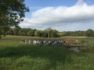 Park Historian Jim Ogden leading a hike. The park historian pointing across a grassy field while a crowd looks on