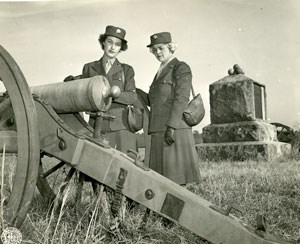 Two female soldiers with a monument and a cannon