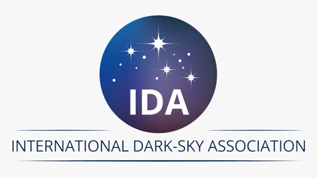 International Dark Sky Association logo (IDA). A dark colored circular image with white star symbols and letters spelling out International Dark-Sky Association underneath
