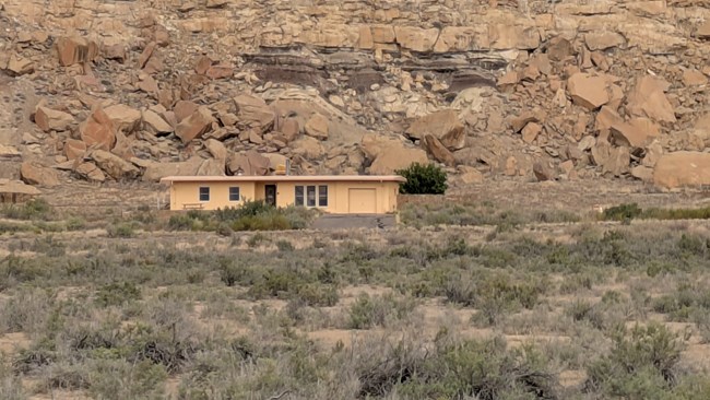 A modern photo of a stucco house sitting in front of a large canyon wall.