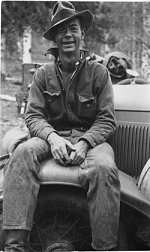 A young man smiling while sitting on a wheel of a car.