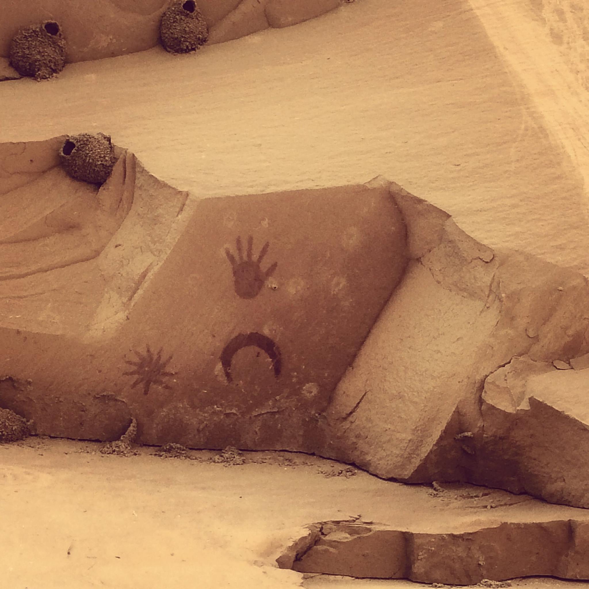 A painted pictograph showing a five-fingered hand print, crescent moon, and sun with rays. It is thought this pictograph represents the Chacoan peoples' observaiton fo the supernova event in 1054.