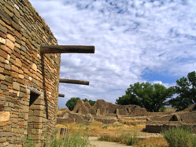 Walls of a reconstructed round masonry kiva, with remains of ancient walls in the background.