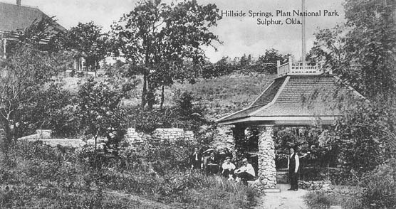 An old black and white image of a stone pavilion on a hillside with people standing next to it.