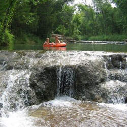 Two boys floating down the creek towards a small waterfall