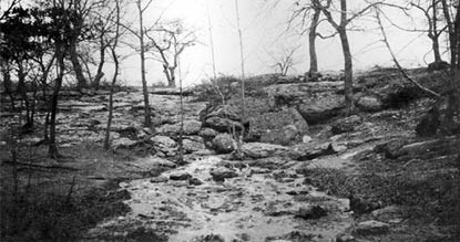 Black and white photograph of spring water flowing over earth and rocks