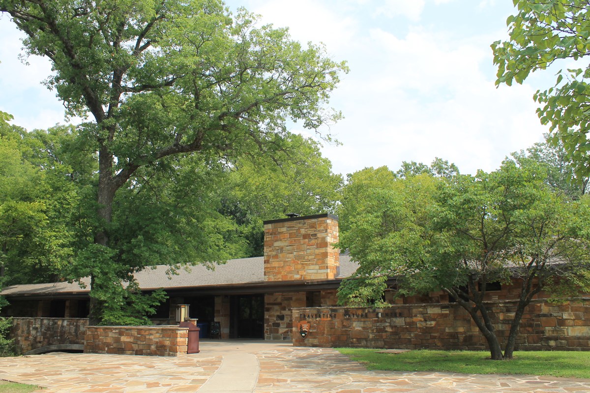 A stone midcentury style building stretches across the bottom of the image. Trees tower above.