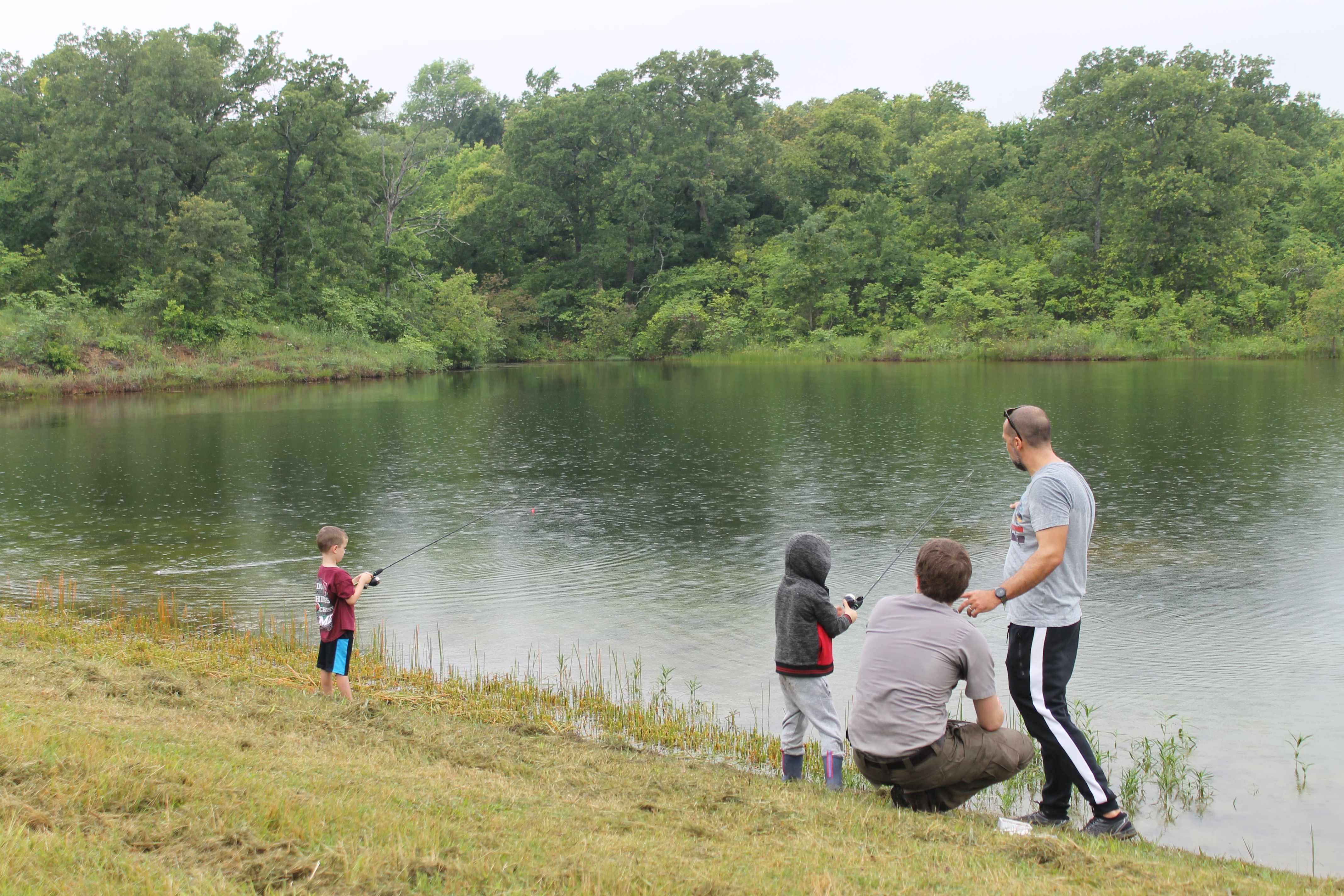 Two children fish along a lakeshore while two adults assist.
