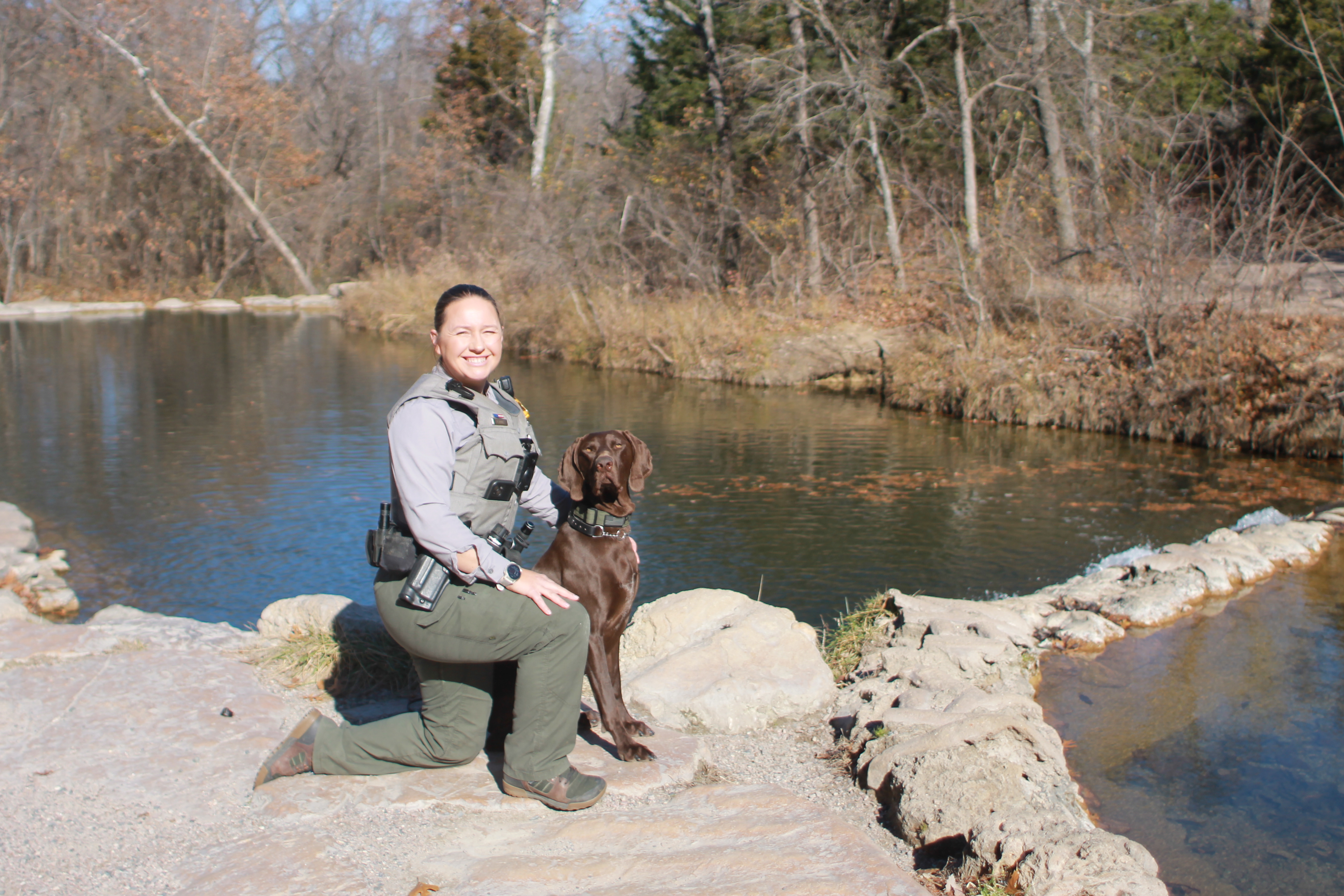 A law enfocement ranger kneels next to a brown dog