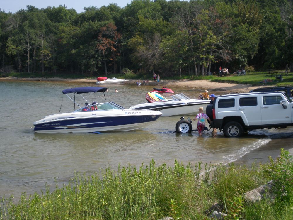 boat at lake of the arbuckles - NPS Photo An SUV with a boat on a trailer is backed into the water at a lakeshore. Several people are around the boat in the water, and another boat is being launched in the background.