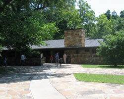 A family exiting a long stone building underneath green trees