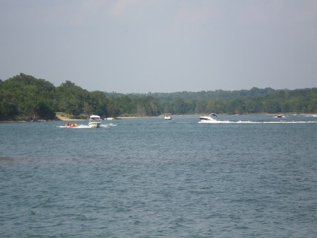 Eight different boats, some on the shore and some speeding across the water, including at least two pulling tubes with people on them.