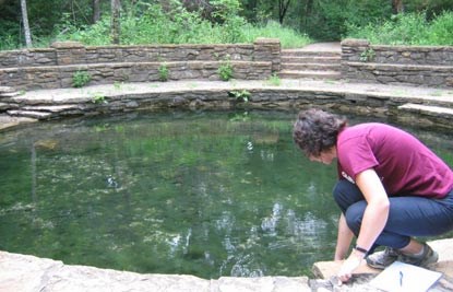 Woman putting her fingers into a circular spring of water.