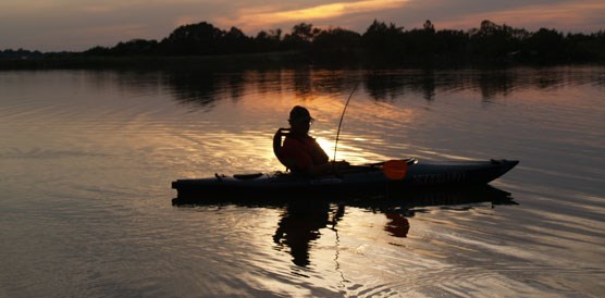 A person in a kayak on a lake at sunrise.